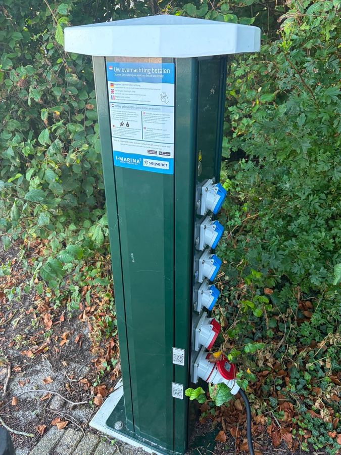 Stroomzuil op een camperterrein met QR-codes voor stroom en water